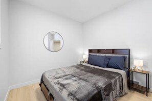 A bedroom with a bed, a round mirror, two bedside tables with lamps, and a wooden floor.