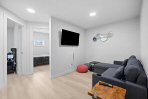 A modern living room with a grey sofa, a wooden coffee table, and a TV mounted on the wall.