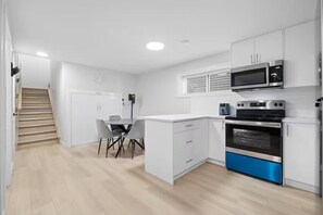 A modern kitchen with white cabinets, a blue oven, and a microwave. There is a dining area with a table and chairs.