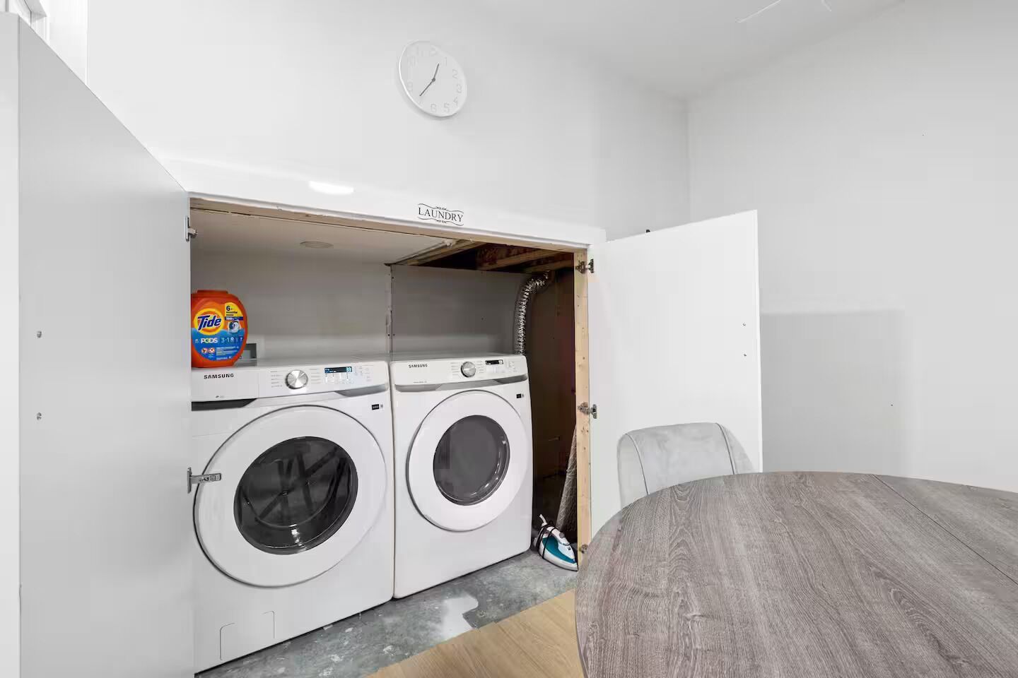 Une petite buanderie équipée de deux machines à laver Samsung, d’une bouteille de lessive Tide et d’une horloge murale.