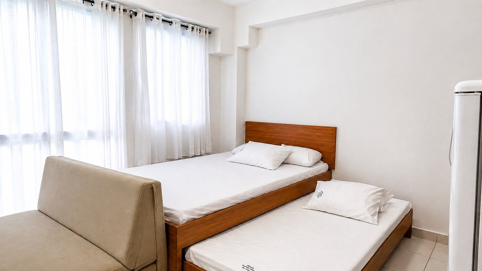 Habitación de hotel con dos camas individuales, un sofá y un refrigerador.