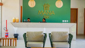A reception area with a green wall, two receptionists, a fire extinguisher, and a seating area with two chairs. - FlatManaBeach (Ipojuca)