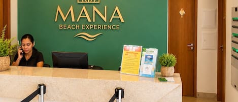 A reception desk with a sign reading 'MANA BEACH EXPERIENCE' and a clock on the wall.