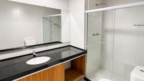 Un baño moderno con lavamanos de encimera negro, cabina de ducha de cristal y paredes cubiertas de azulejos blancos.