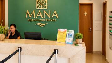A reception desk with a sign reading 'MANA BEACH EXPERIENCE' and a clock on the wall.