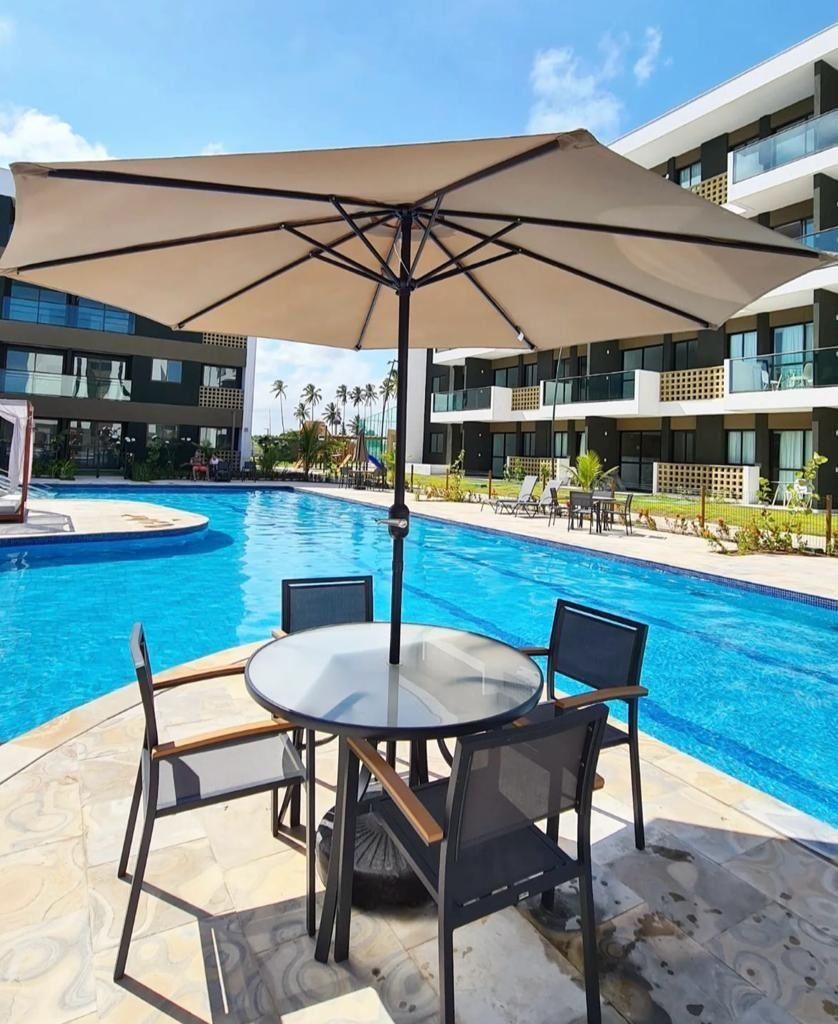 Zona de piscina con mesa y sillas, una gran sombrilla y un edificio moderno al fondo.