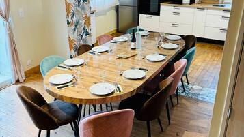 Un coin repas avec une table en bois dressée pour six personnes, entourée de chaises, dans une cuisine moderne dotée de meubles blancs et d’un four encastré.