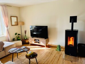 A living room with a TV, sofa, coffee table, and a wood-burning stove. - Chez Coco – 4-Star Family Home with Jacuzzi & Games in Cantal (Mauriac)