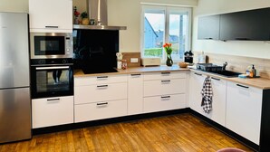 A modern kitchen with built-in appliances, a large window, and a view of the outdoors. - Chez Coco – 4★ Family Home, Jacuzzi & Games, Cantal (Mauriac)