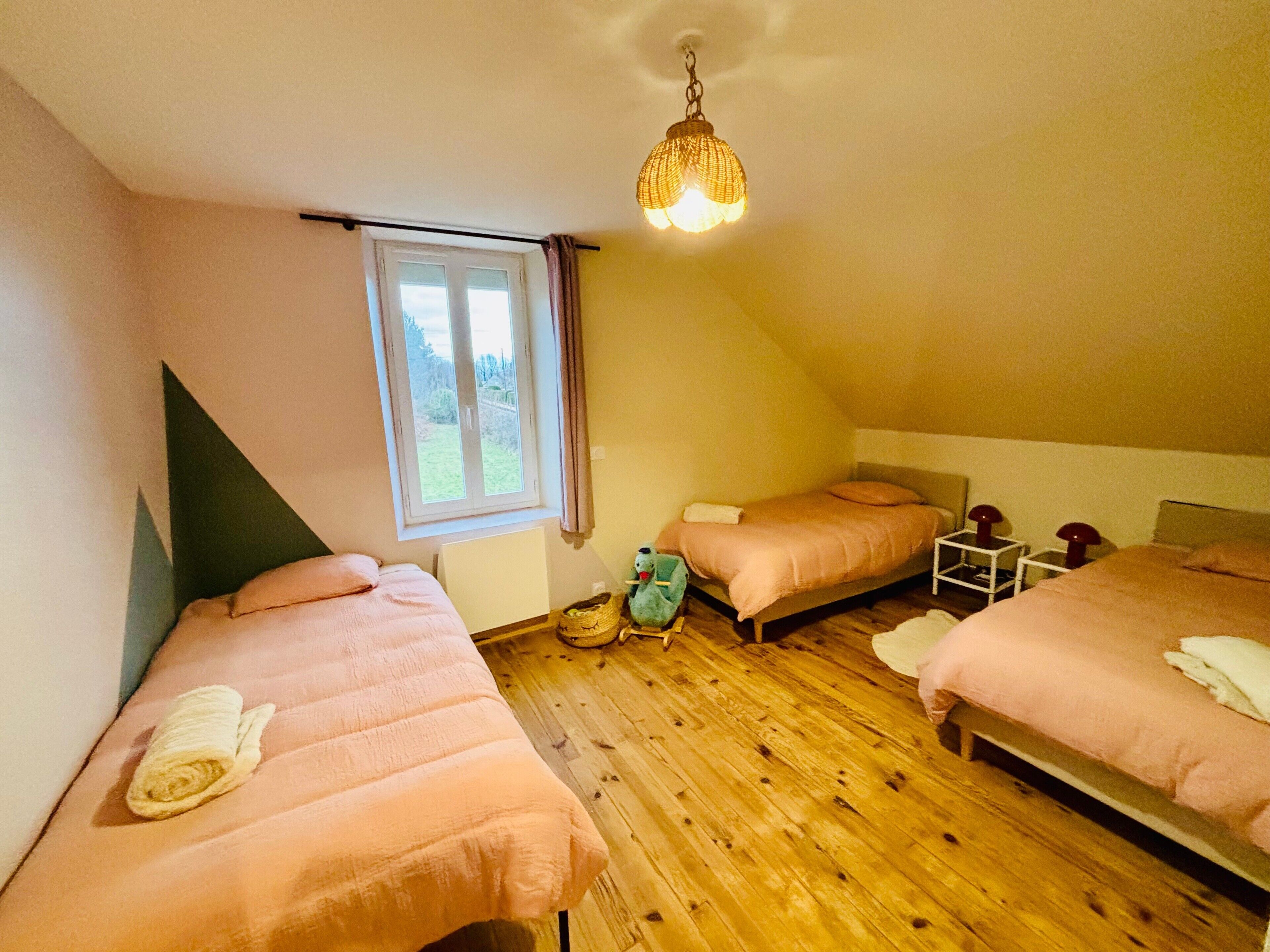 A bedroom with two beds, a window, a ceiling light, and a wooden floor.