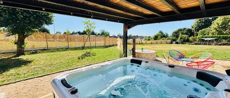 Un jacuzzi bajo una pérgola de madera, con un jardín de césped y sillas al fondo.