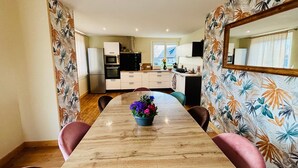 A dining area with a wooden table, chairs, and a floral-patterned wall. - Chez Coco – 4★ Family Home, Jacuzzi & Games, Cantal (Mauriac)