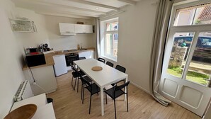 Una cucina compatta con elettrodomestici moderni, una zona pranzo con tavolo bianco e sedie nere, e un'ampia finestra con vista sull'esterno.