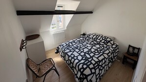 Una camera da letto con soffitto a falde, un letto con copriletto decorato, una sedia, un tavolino e una finestra con vista sull'esterno.