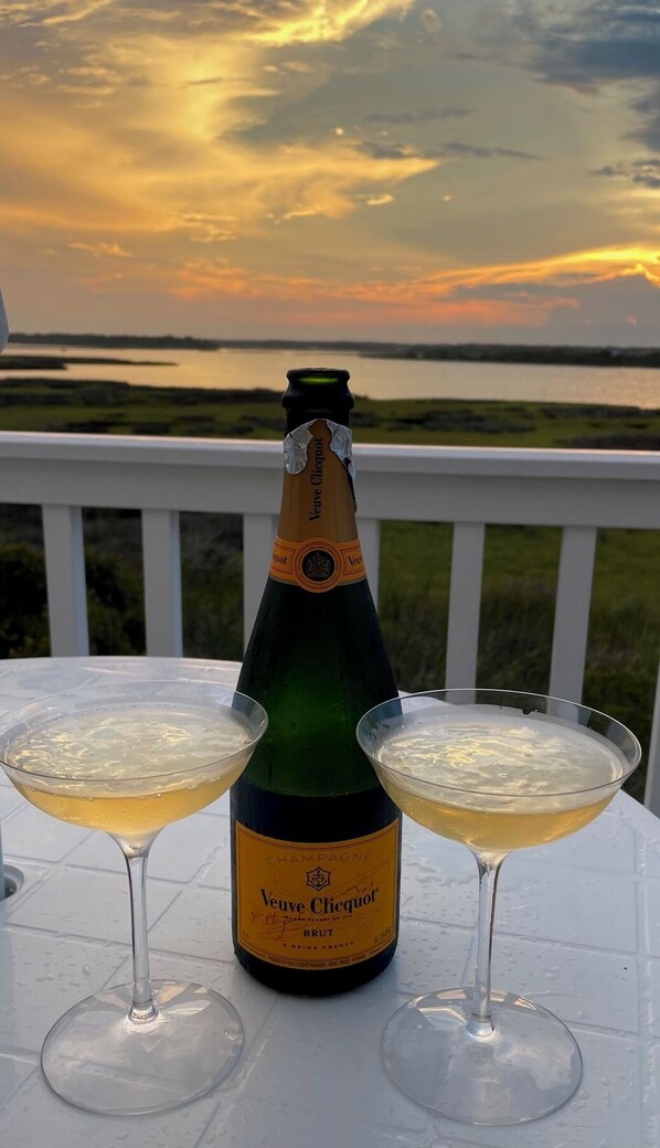 A bottle of Veuve Clicquot champagne and two glasses on a table with a view of a sunset over a body of water. - Volare at the Sea
3-bedroom townhome with Ocean View and Pool (North Topsail Beach)