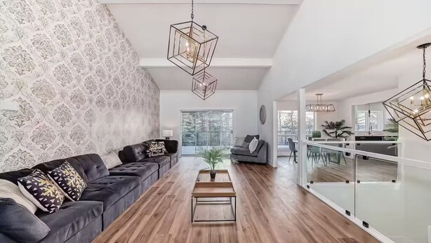 A modern living room with a dark leather sofa, a wooden coffee table, and geometric pendant lights. - Walkout Bungalow with Pond Views (Delacour)