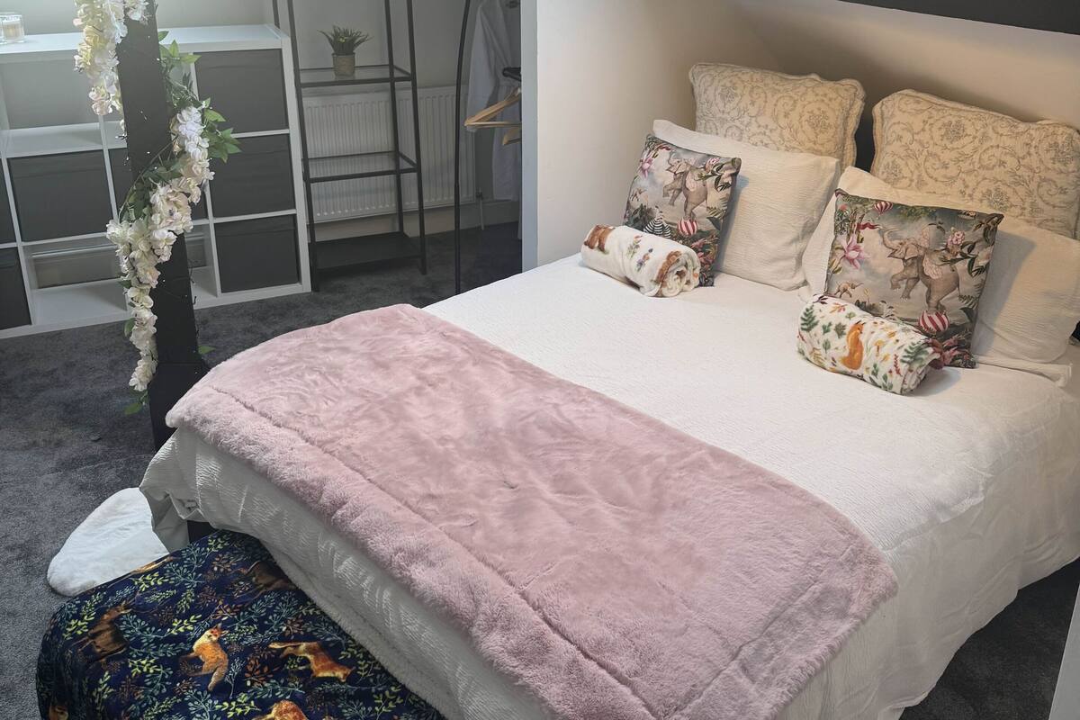 Une chambre avec un puits de lumière, un lit agrémenté d’oreillers à motifs, une couverture rose et un banc orné d’un motif de cerf.