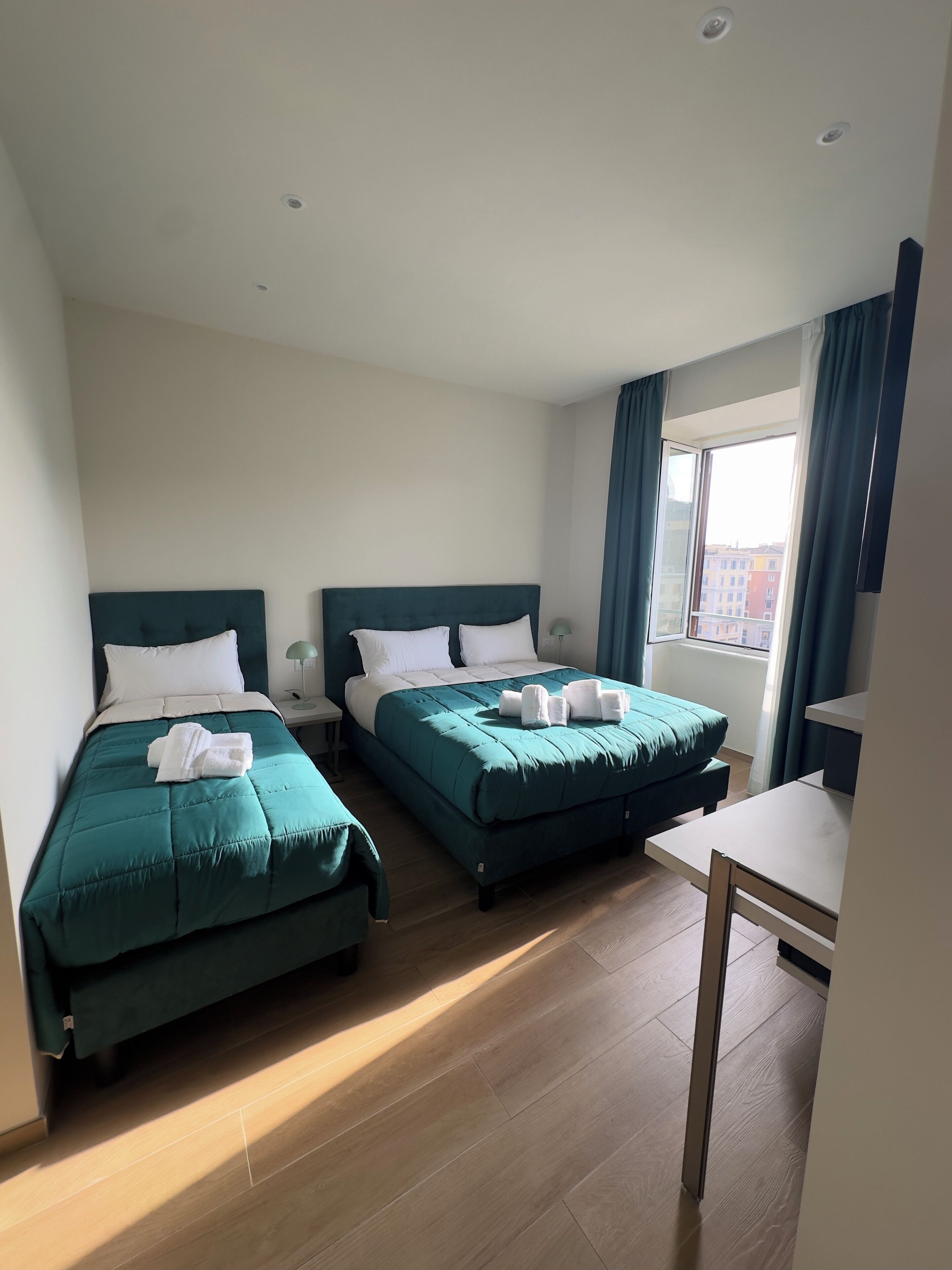 A hotel room with two beds, a desk, and a window with curtains.