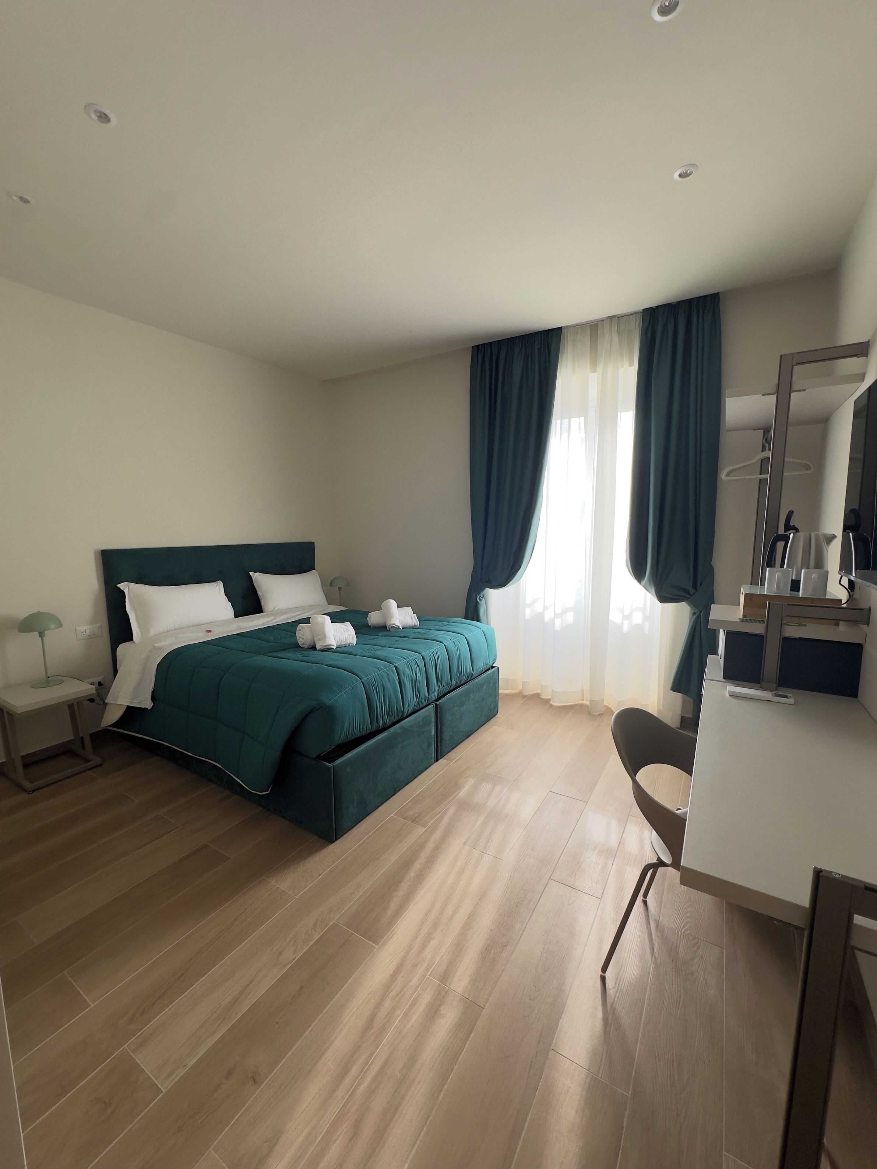 A modern hotel room with a bed, a desk, and a mirror.