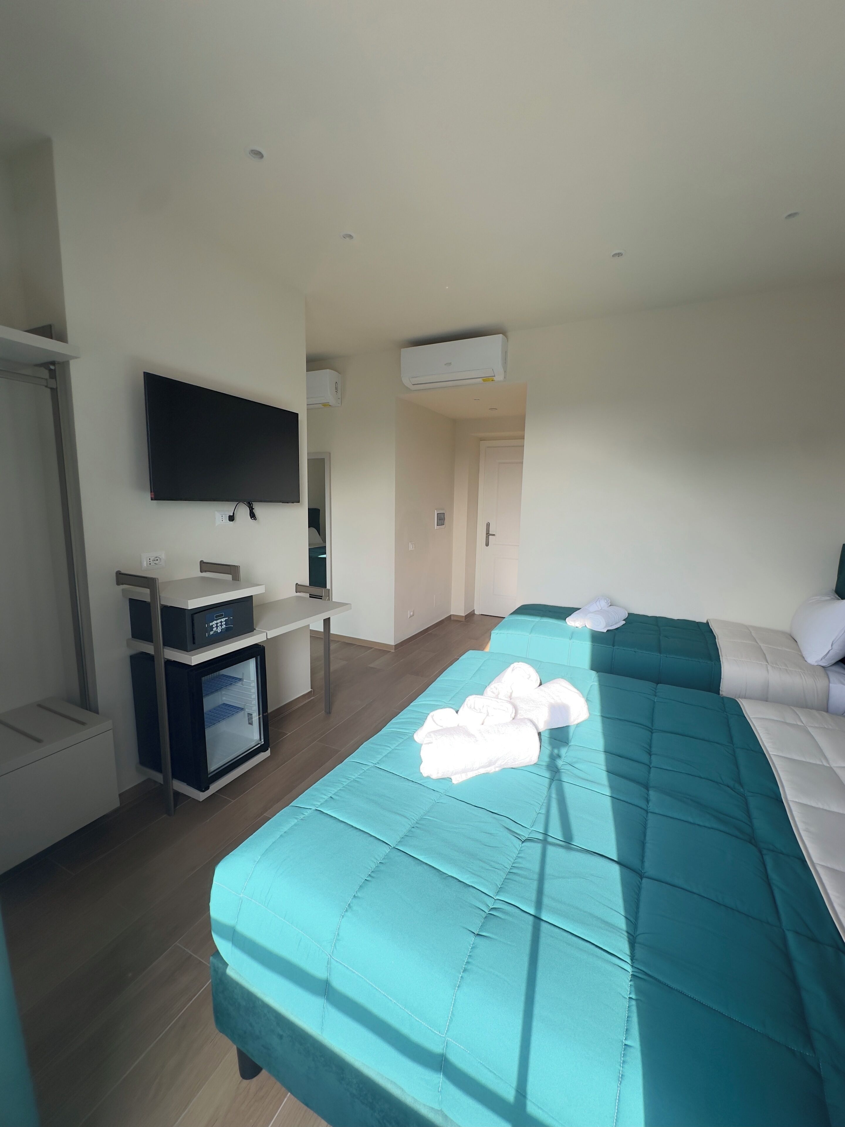 A hotel room with a bed, a TV, a minibar, and an air conditioning unit.
