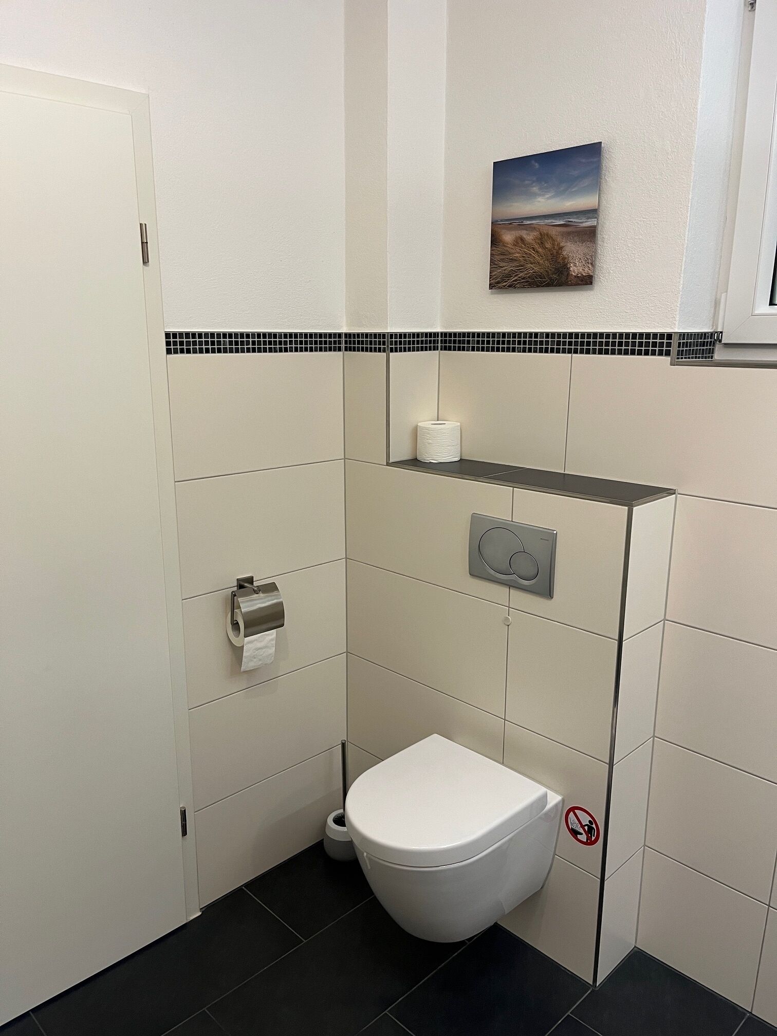 Ein kleines, sauberes Badezimmer mit Toilette, Papierhandtuchspender und einem Handtrockner.