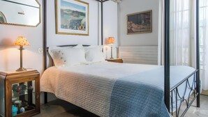 A neatly made bed with a quilted bedspread, two bedside lamps, a wooden cabinet with glass doors, and two framed artworks on the wall.