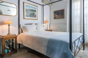 Un lit bien fait, recouvert d’une courtepointe matelassée, deux lampes de chevet, une armoire en bois aux portes vitrées et deux œuvres d’art encadrées accrochées au mur.