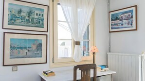 A room with a desk, chair, framed pictures, and a window with curtains.