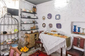 Une pièce avec une table à manger dressée pour un repas, entourée d’étagères remplies de divers ustensiles de cuisine et d’assiettes décoratives.