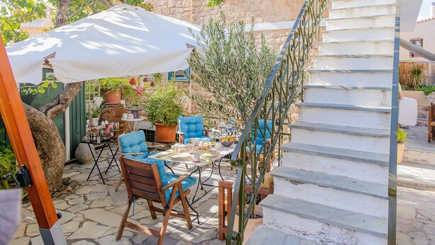 A stone-floored patio with outdoor furniture, a white umbrella, and a staircase.