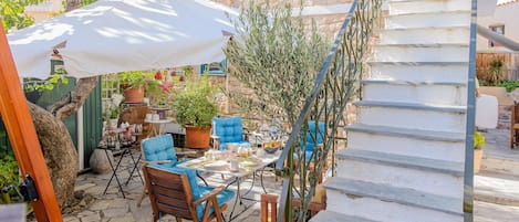 Une terrasse dallée de pierres, avec des meubles d’extérieur, un parasol blanc et un escalier.