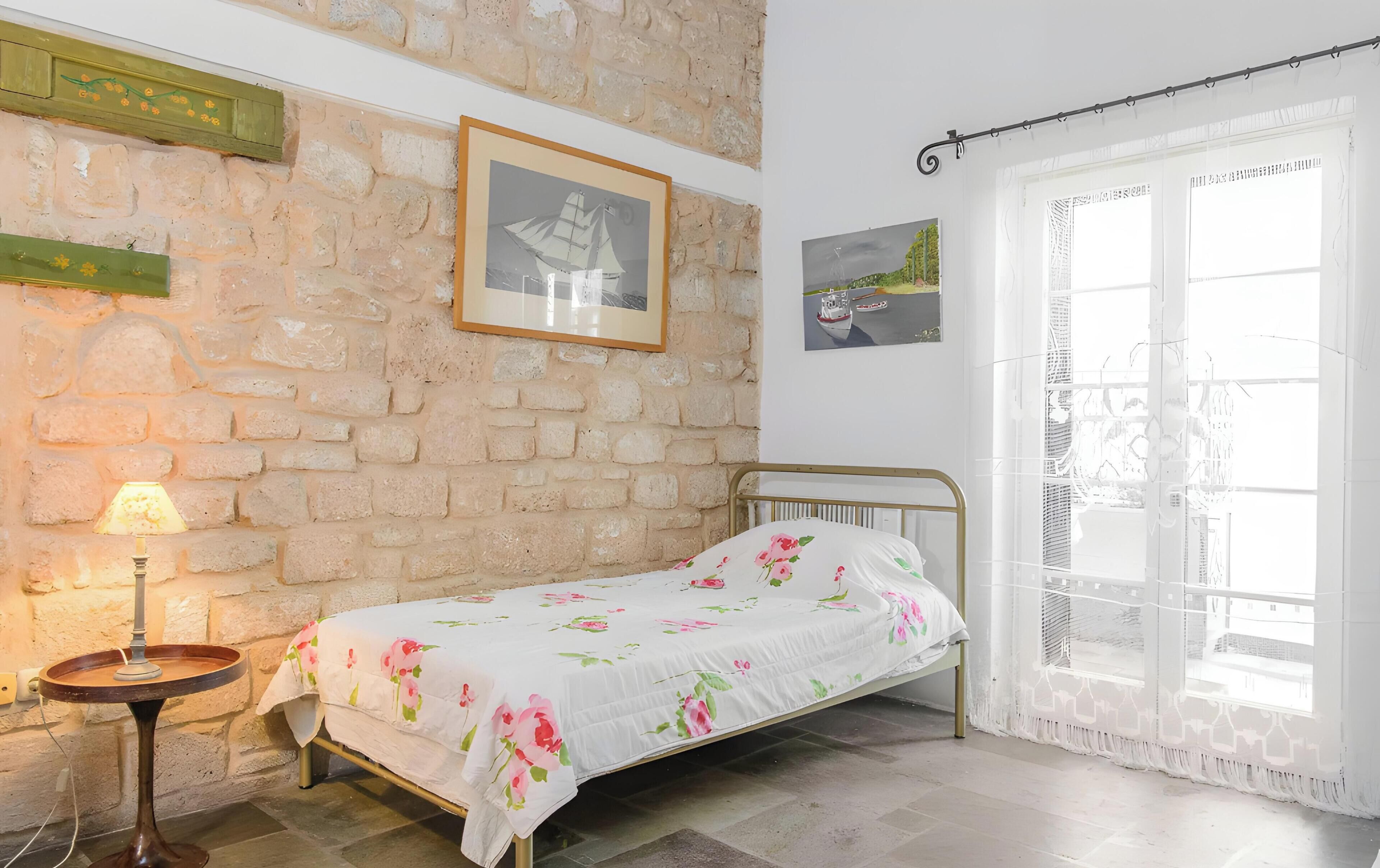 A bedroom with a bed, a lamp, a window with curtains, and a stone wall.