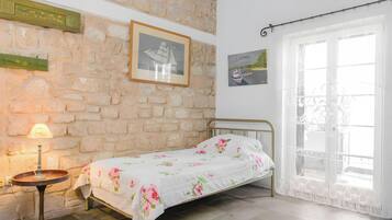 A bedroom with a bed, a lamp, a window with curtains, and a stone wall.