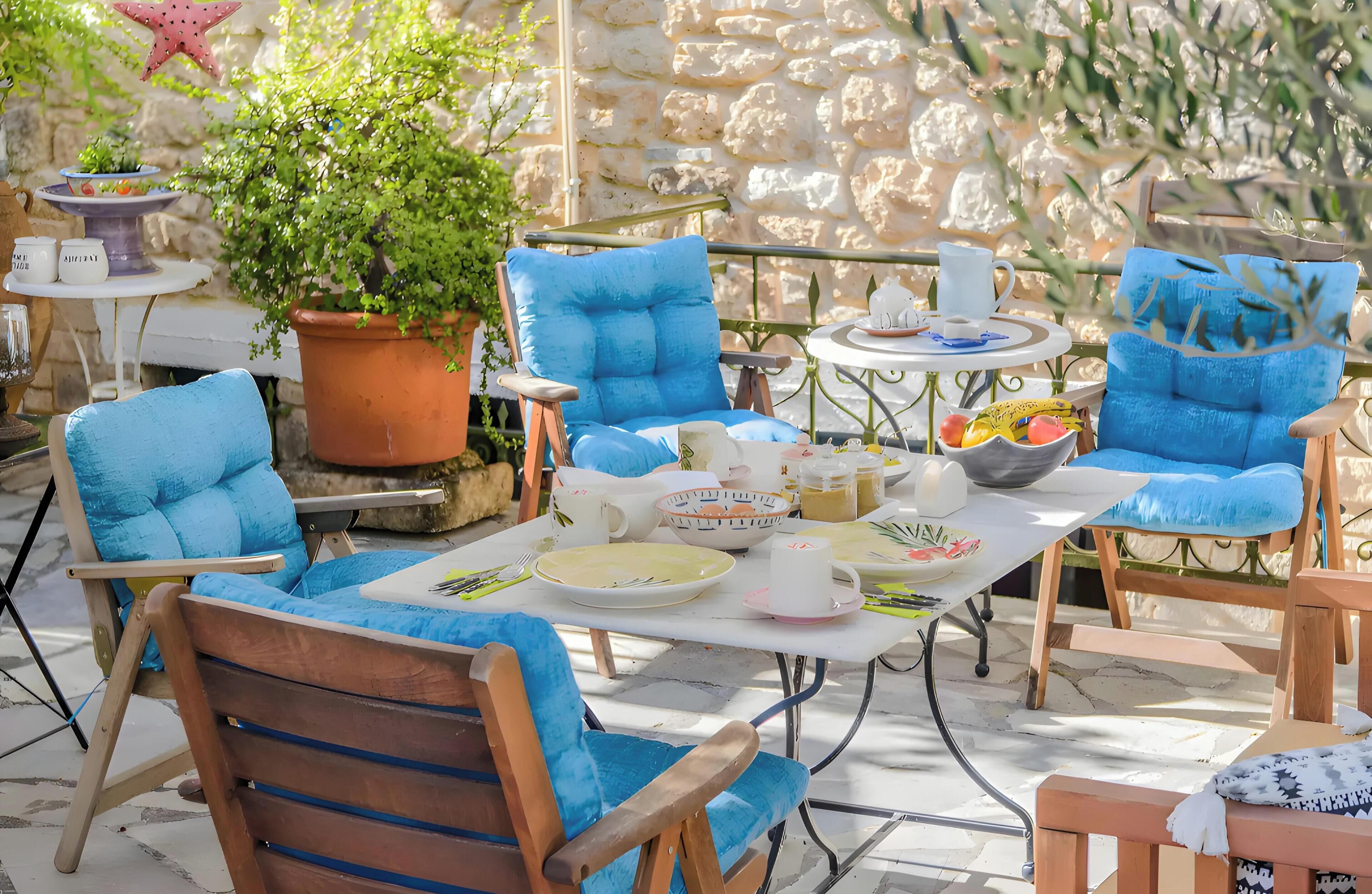 Een terras met blauwe, beklede stoelen, een tafel met borden, kopjes en een bloempot.