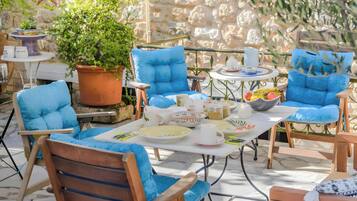 Een terras met blauwe, beklede stoelen, een tafel met borden, kopjes en een bloempot.