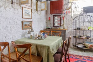 A dining area with a table set for four, surrounded by wooden chairs. A red cabinet and a metal birdcage with decorative items are visible in the background. - Apartment in 'Unit 6' Hotel with Private Terrace, Wi-Fi and Air Conditioning (Egina)