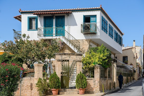 A two-story building with a stone facade, blue shutters, and a balcony with metal railings.