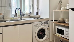 A modern kitchen with a built-in washing machine, a microwave, and a sink with a window above it.