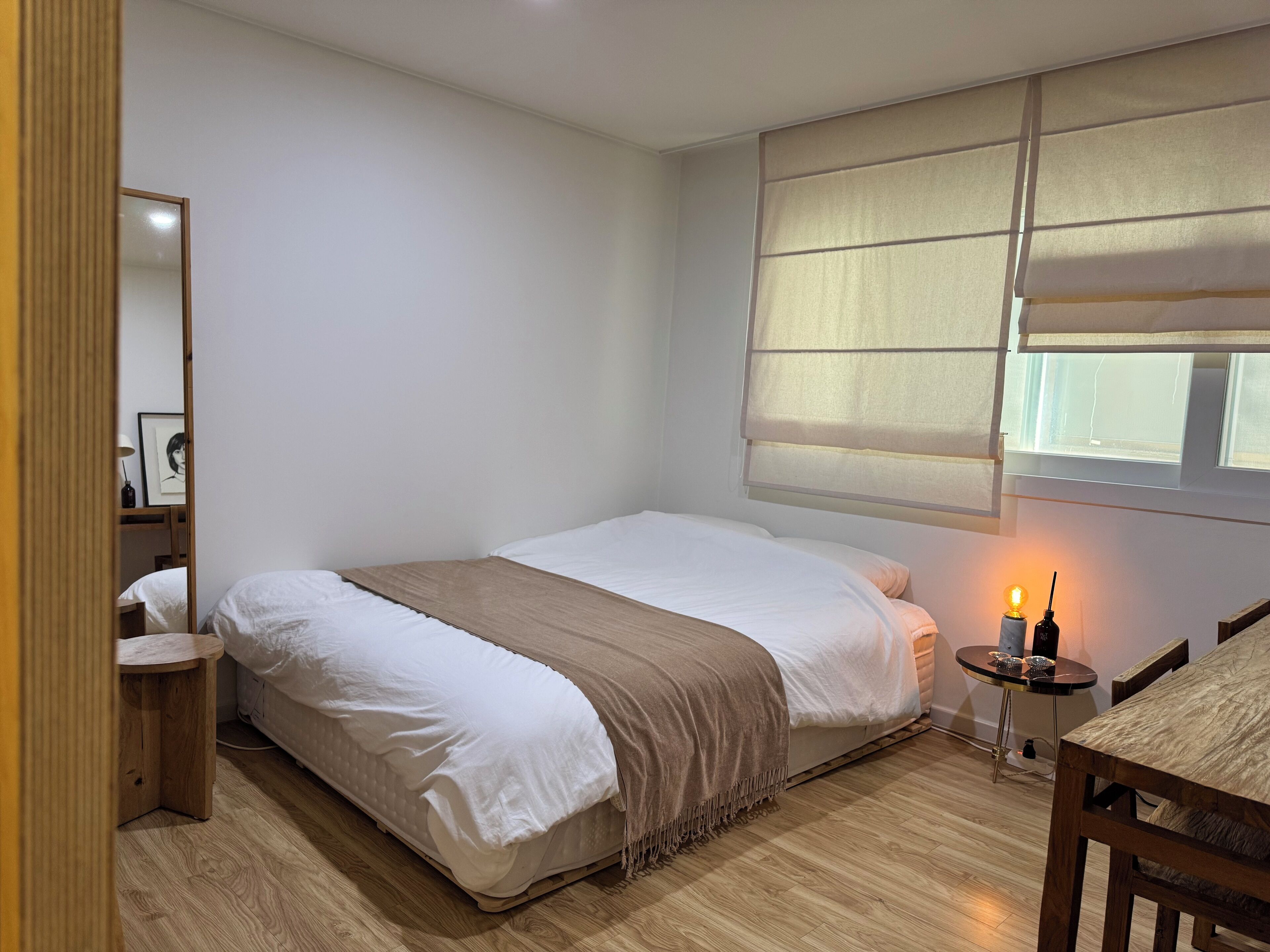 Un dormitorio con cama, mesita de noche, lámpara y ventana con persianas.