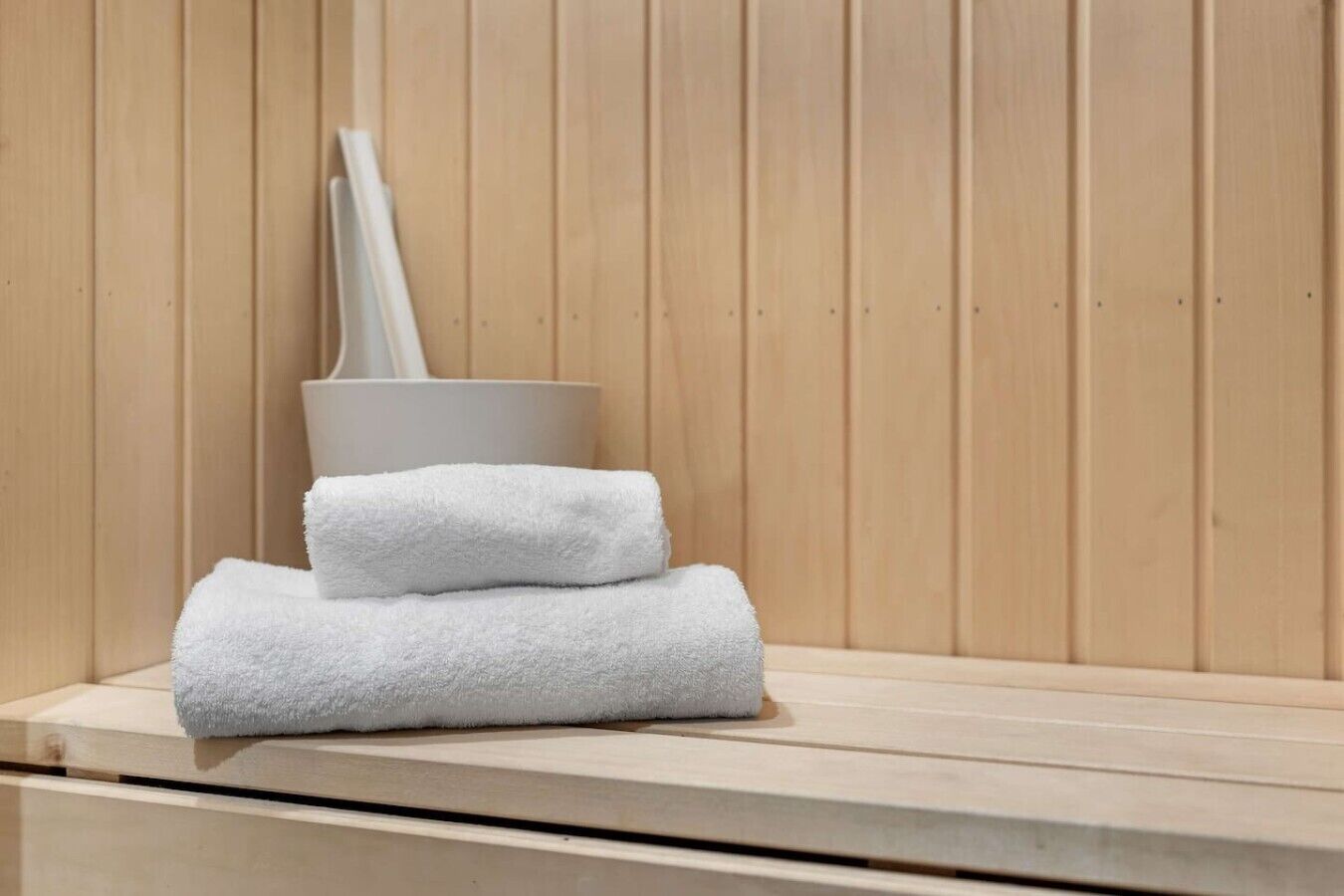 Eine Sauna mit einer Holzbank, einem weißen Handtuch und einer weißen Saunabürste.