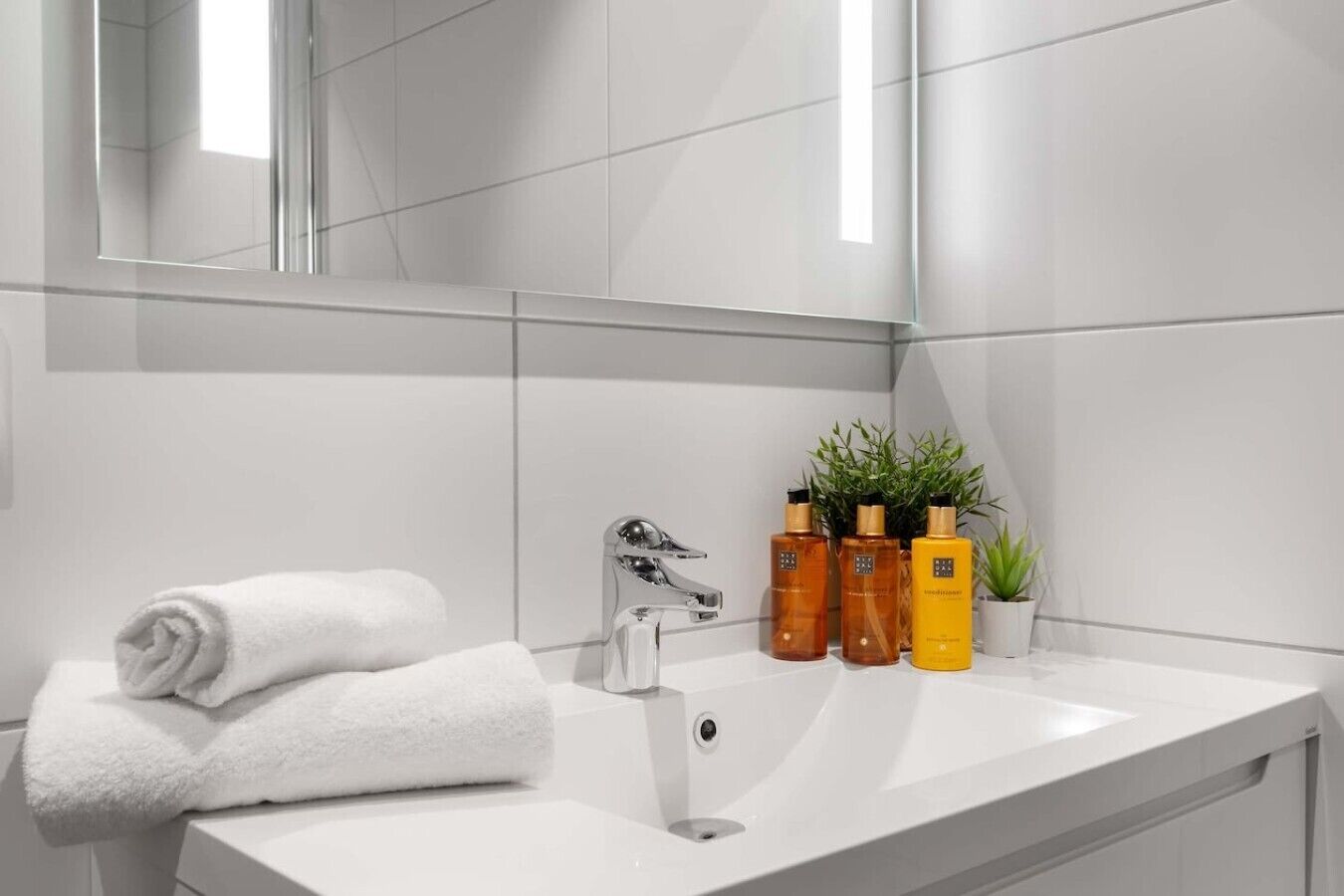 A bathroom with a white sink, a mirror, and a towel. There are three bottles of toiletries on the sink.