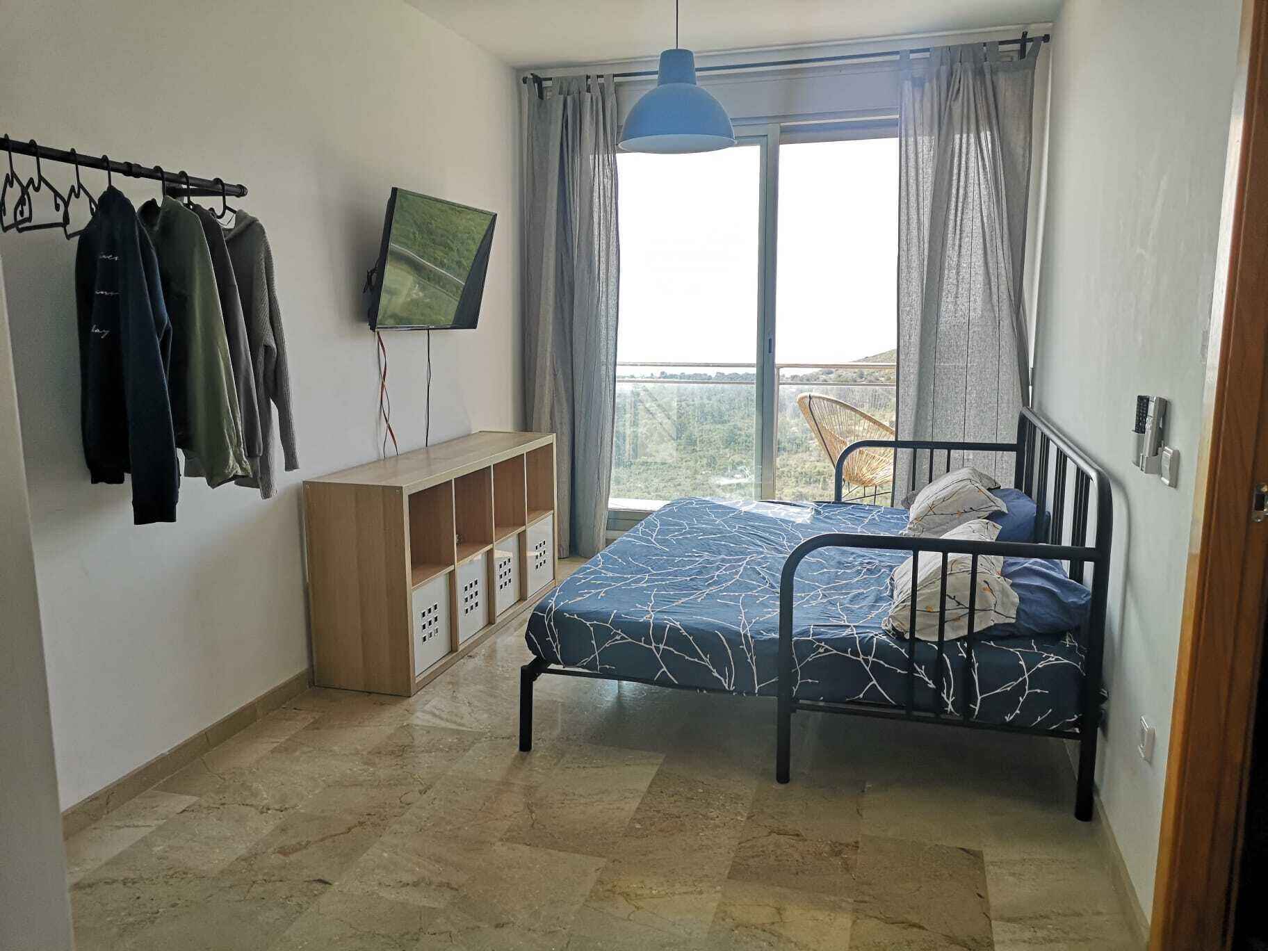 Quarto com cama, televisão na parede, guarda-roupa e varanda com vista.