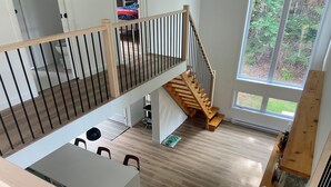 Ein großzügiges Loft-Apartment mit Holztreppe, Essbereich und einem großen Fenster mit Blick ins Freie.
