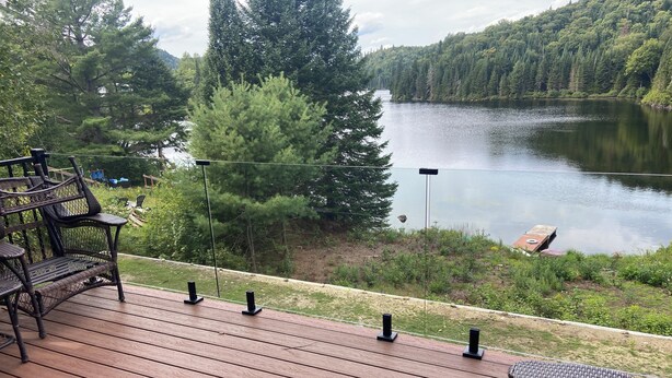 Eine Holzterrasse mit Gartenmöbeln mit Blick auf einen See, umgeben von dichtem Baumbestand.