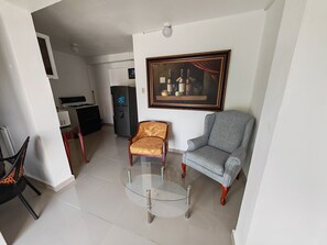 Ein Wohnzimmer mit einem Glastisch, zwei Stühlen, einem Kühlschrank und einem gerahmten Bild an der Wand.
