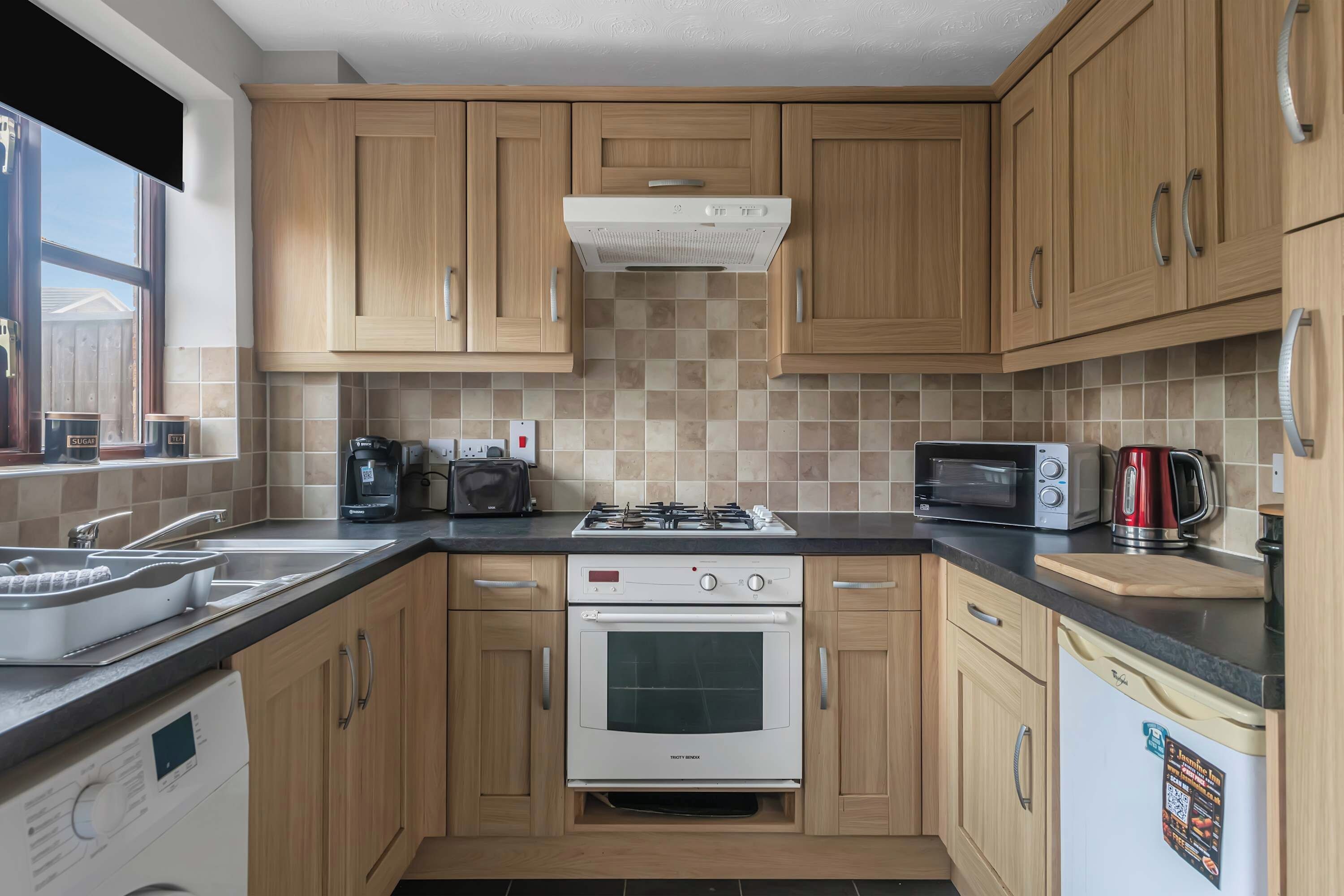 A modern kitchen with wooden cabinets, a gas stove, a built-in oven, a microwave, and a kettle.