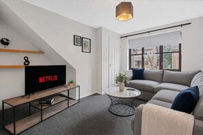 A modern living room with a flat-screen TV, a sofa, a coffee table, and a staircase. - Large Drive and Garden (Lenton)