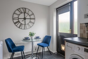 A modern kitchen with a large wall clock, a dining table with chairs, a radiator, and a washing machine. - Large Drive and Garden (Lenton)