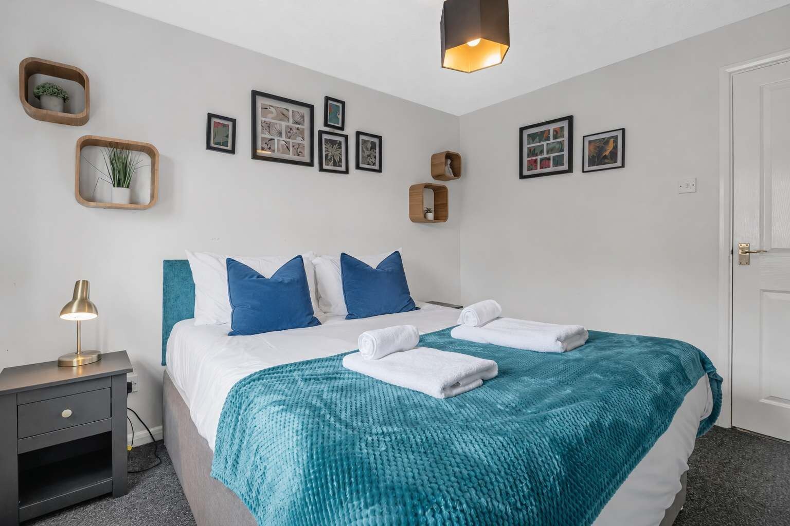 A neatly arranged hotel room with a bed, a bedside table with a lamp, and a wall adorned with framed pictures.