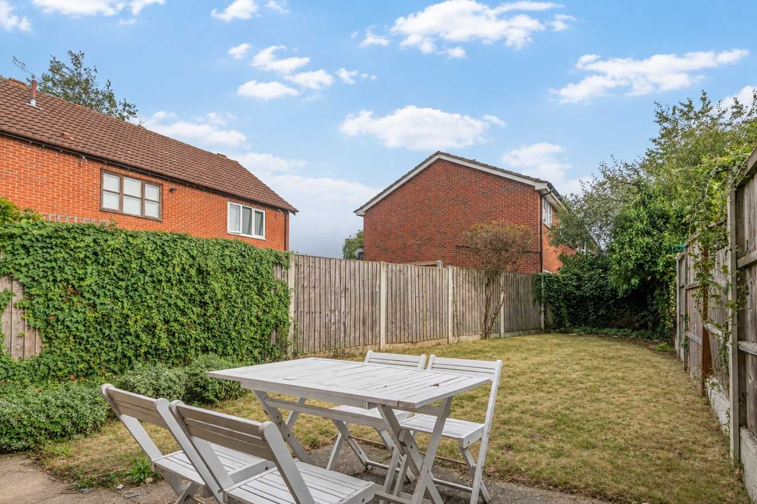 A backyard with a picnic table and chairs, surrounded by a wooden fence and a brick house.